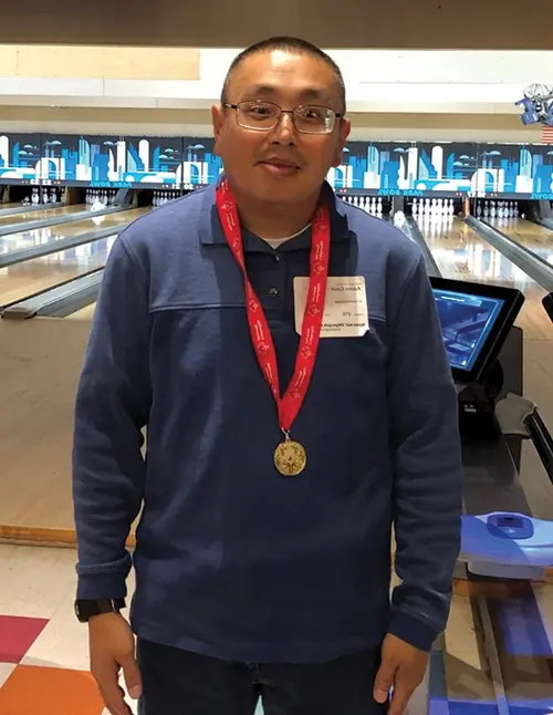 at bowling alley a man wearing glasses standing wearing a medal