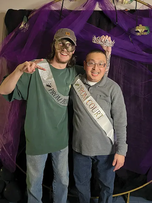 two men standing, smiling, wearing prom award ribbons