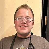 a man wearing glasses and apron, smiling at camera