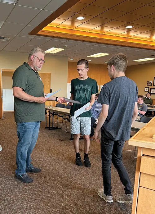 a teacher on the left and two students on the right, standing in classroom