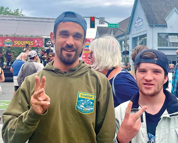Two men smiling at camera holding up hand peace signs.