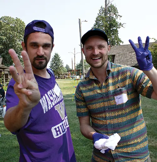 Two men in the field, smiling, wearing baseball caps, holding up three fingers sign