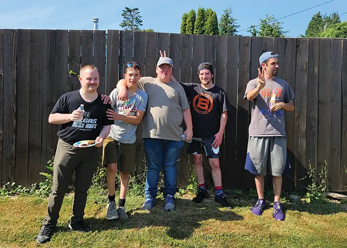 five men standing outside on grass in front of the fence, smiling