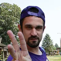 a man wearing baseball cap, holding three fingers up, looking at the camera