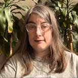 a woman wearing glasses. background has house plants.