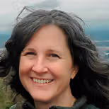 a woman smiling, background is landscape with blue sky