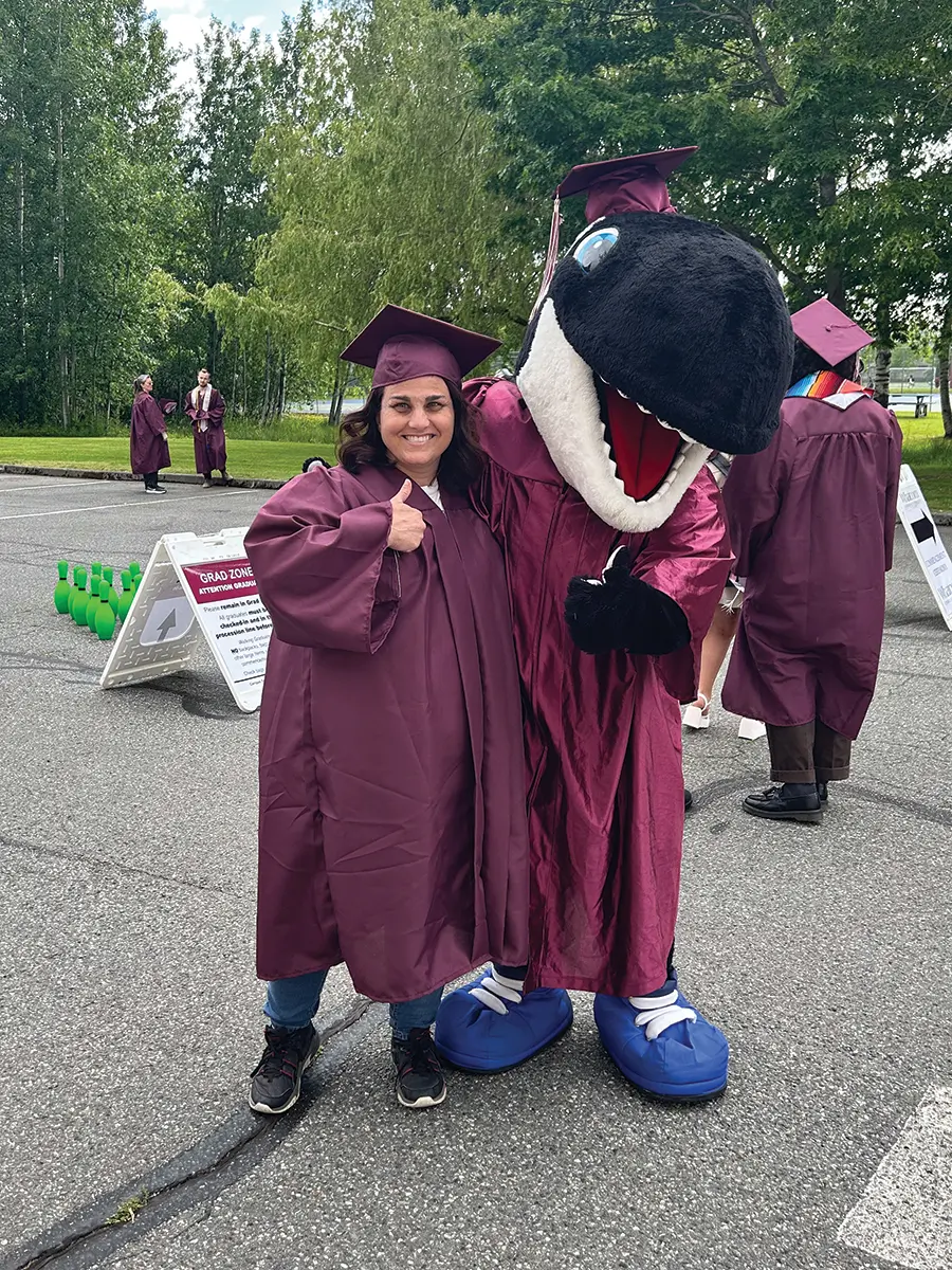 Hilary standing with a person who is wearing a dinosaur costume, thumbs up.