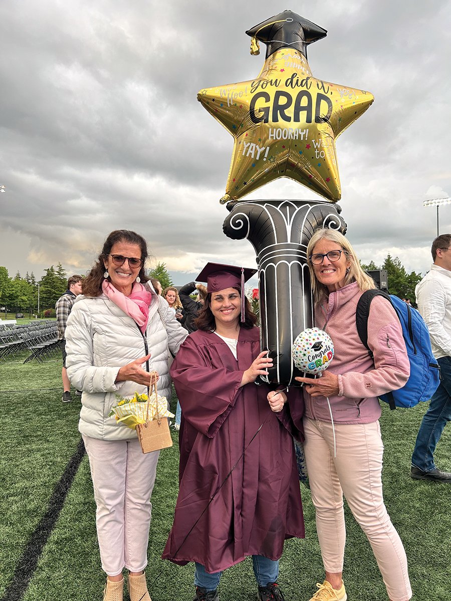 Hilary standing with two ladies, smiling, holding a graduation baloon.
