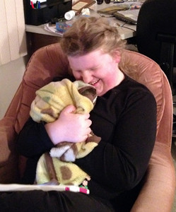 A young woman sitting on a chair, hugging a blanket and smiling.