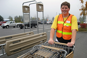 A man pushing shopping carts, wearing an orange/yellow safety vest, working, smiling.