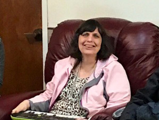 A woman wearing a pink long sleeve shirt, sitting on a chair, smiling at camera.